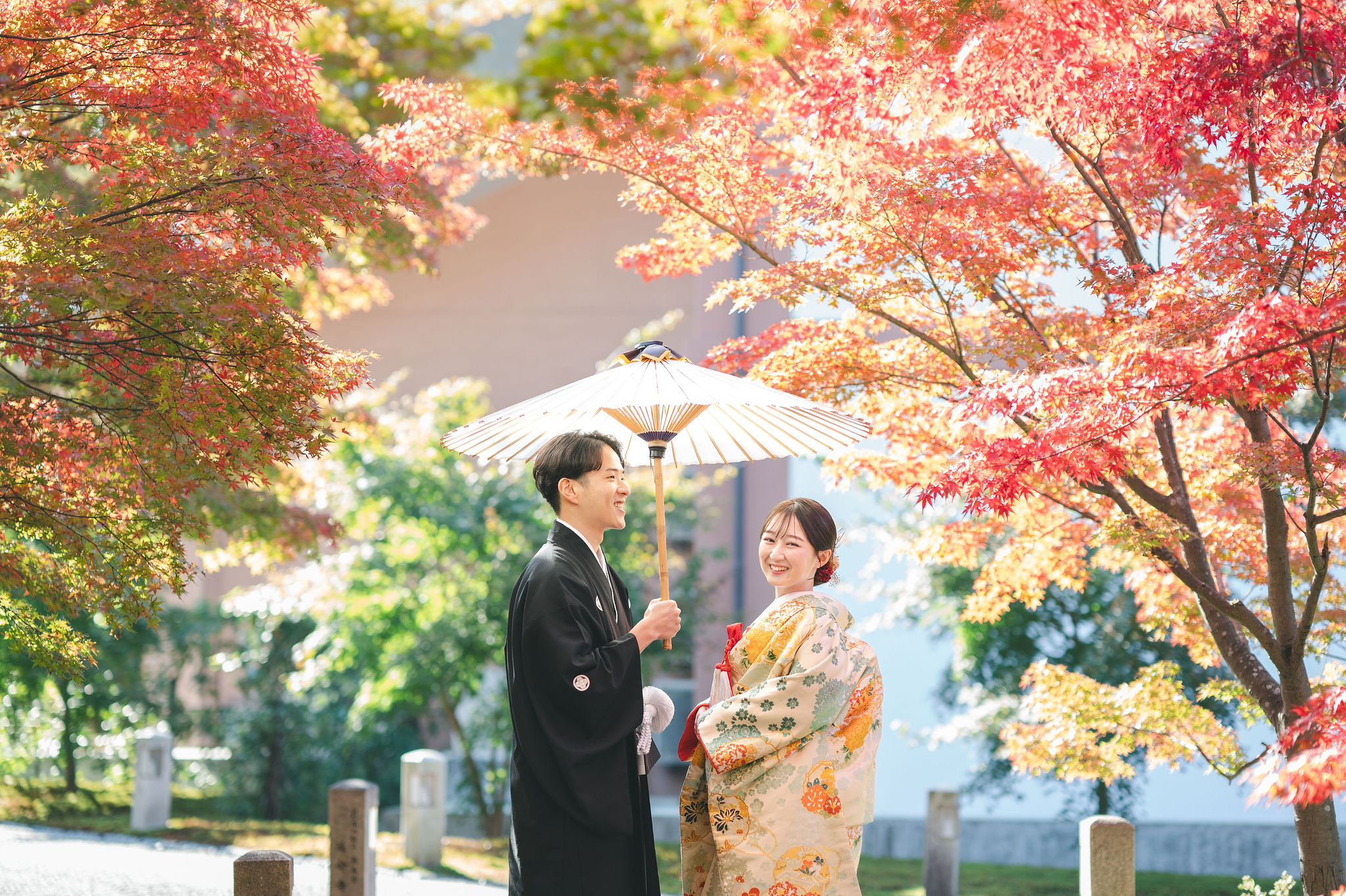 智積院の紅葉に囲まれ番傘を持って微笑み合う和装新郎新婦の前撮り写真