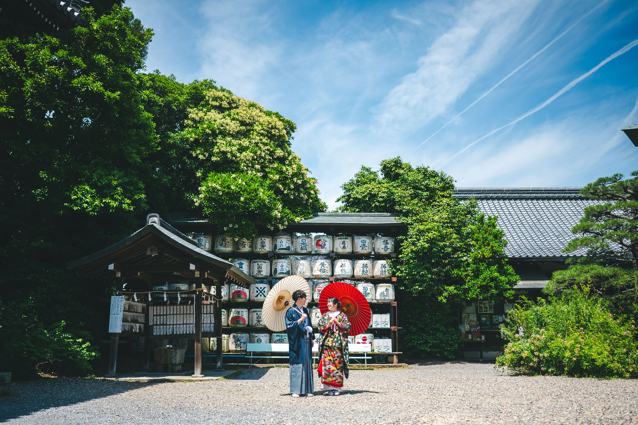 酒樽を背景に和傘を持つ和装の新郎新婦